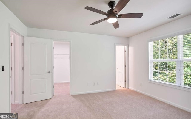 unfurnished bedroom with a spacious closet, light carpet, baseboards, visible vents, and a ceiling fan