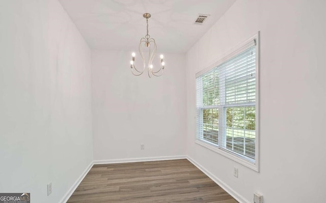 unfurnished dining area with dark wood-style floors, visible vents, a chandelier, and baseboards
