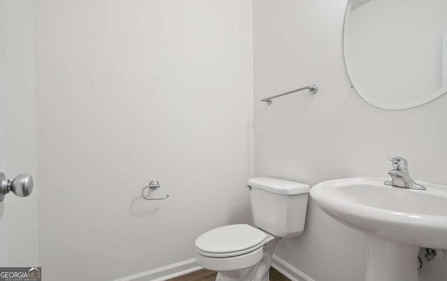 bathroom with baseboards, wood finished floors, toilet, and a sink