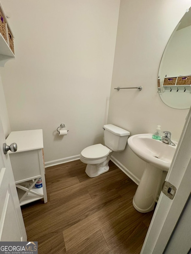 half bathroom featuring wood finished floors, toilet, and baseboards