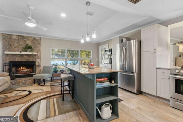 kitchen with light wood finished floors, open shelves, a fireplace, white cabinets, and appliances with stainless steel finishes