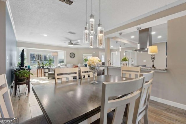 dining space with visible vents, baseboards, light wood-type flooring, a textured ceiling, and a ceiling fan