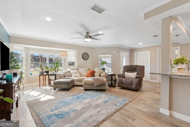 living area featuring visible vents, light wood-style flooring, a textured ceiling, and baseboards