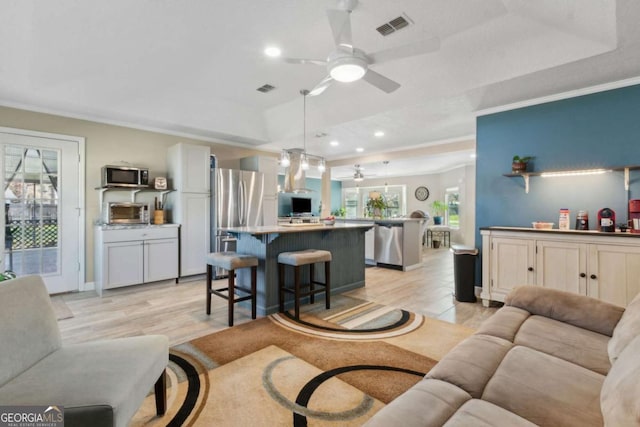 living area with visible vents, ceiling fan, ornamental molding, light wood-style flooring, and a raised ceiling