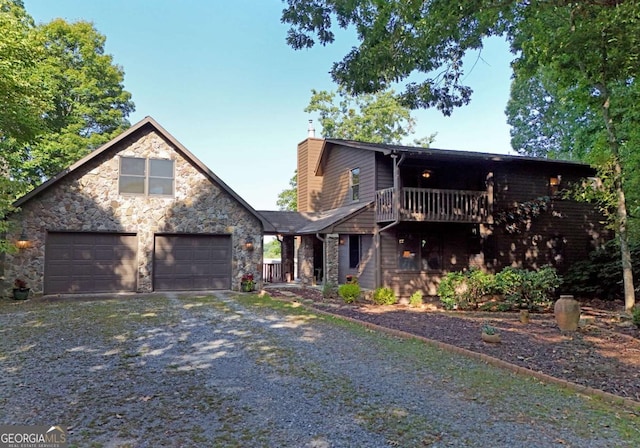 view of front of house with stone siding, gravel driveway, an attached garage, a balcony, and a chimney