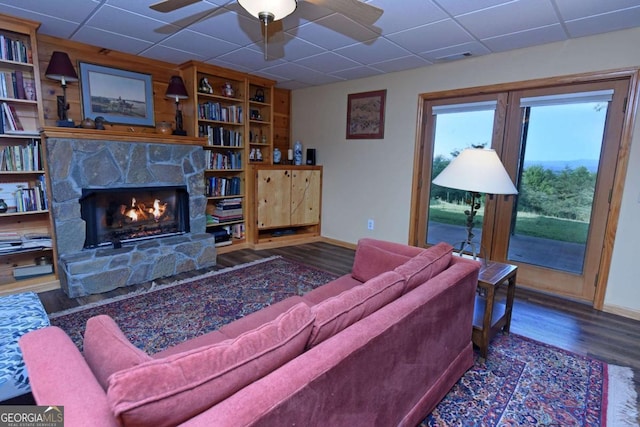 living area featuring baseboards, wood finished floors, a stone fireplace, and ceiling fan