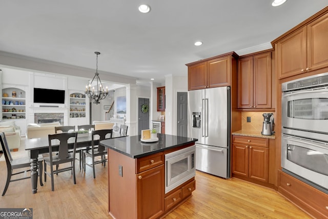 kitchen with a fireplace, light wood-style floors, appliances with stainless steel finishes, crown molding, and a chandelier