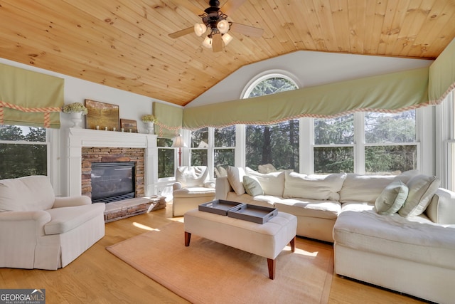 living room with wood ceiling, lofted ceiling, a stone fireplace, wood finished floors, and a ceiling fan