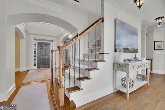 entryway featuring arched walkways, crown molding, baseboards, and wood finished floors