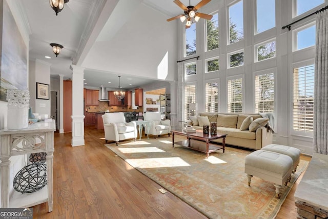 living room with plenty of natural light, light wood-style flooring, ceiling fan with notable chandelier, and ornate columns