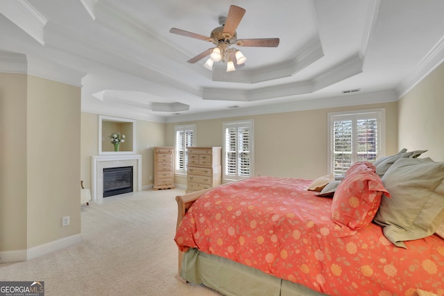 carpeted bedroom with visible vents, baseboards, a tray ceiling, ornamental molding, and a glass covered fireplace