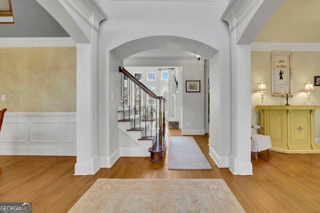 foyer with arched walkways, wainscoting, stairs, and wood finished floors