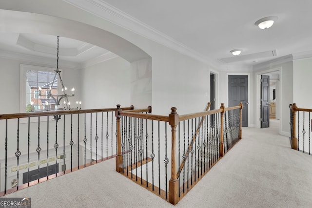 hallway with a tray ceiling, carpet floors, an upstairs landing, ornamental molding, and an inviting chandelier