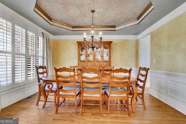 dining area featuring a notable chandelier, visible vents, a tray ceiling, and wood finished floors