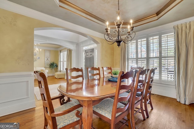 dining area with a wainscoted wall, a notable chandelier, a tray ceiling, wood finished floors, and arched walkways