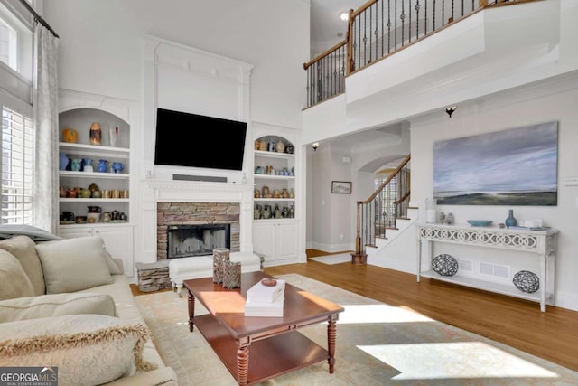 living area with built in features, wood finished floors, stairway, a fireplace, and a towering ceiling