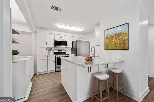 kitchen with visible vents, appliances with stainless steel finishes, a peninsula, white cabinetry, and a sink