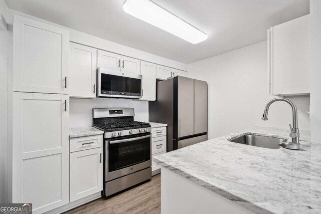 kitchen featuring light wood-style flooring, a sink, light stone counters, stainless steel appliances, and white cabinets