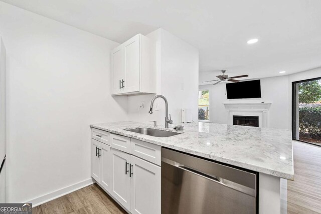 kitchen with a sink, light stone counters, stainless steel dishwasher, a peninsula, and white cabinets