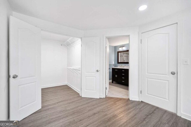 unfurnished bedroom featuring ensuite bathroom, baseboards, and wood finished floors