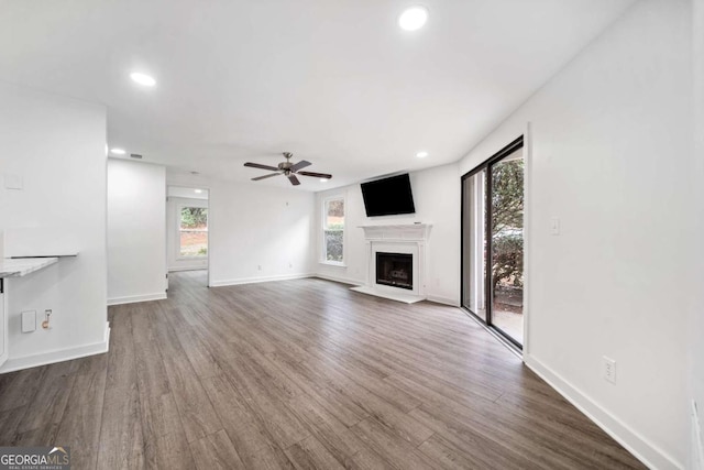 unfurnished living room featuring recessed lighting, a fireplace with raised hearth, baseboards, and wood finished floors