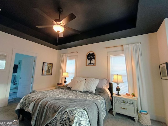 carpeted bedroom with a raised ceiling and ceiling fan