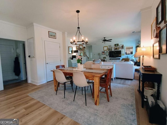 dining room featuring light wood finished floors, ceiling fan with notable chandelier, baseboards, and ornamental molding