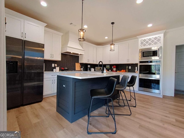 kitchen with light wood finished floors, white cabinets, stainless steel appliances, and premium range hood