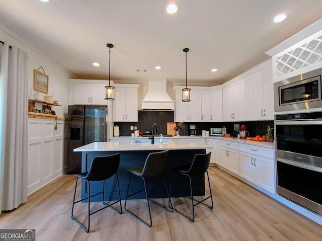 kitchen featuring white cabinetry, custom exhaust hood, light wood-style floors, and appliances with stainless steel finishes