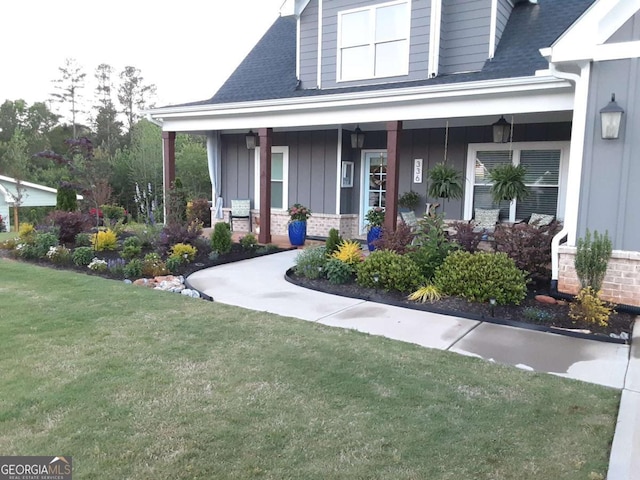 view of exterior entry with a porch, a yard, board and batten siding, a shingled roof, and brick siding