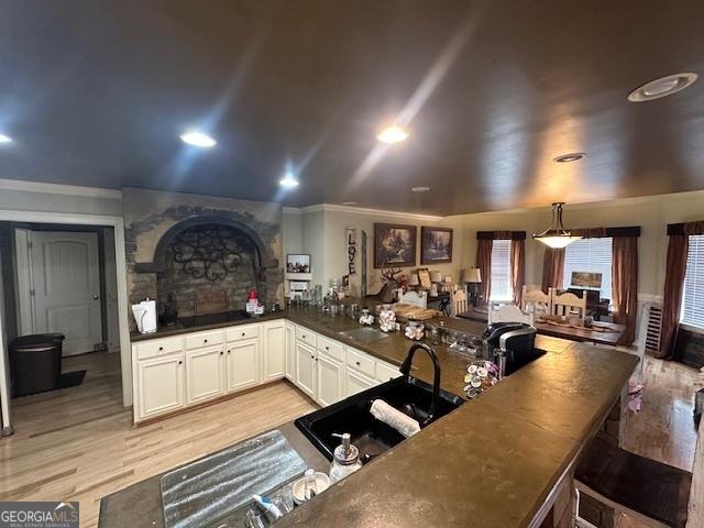 kitchen with ornamental molding, a sink, dark countertops, white cabinetry, and light wood-style floors