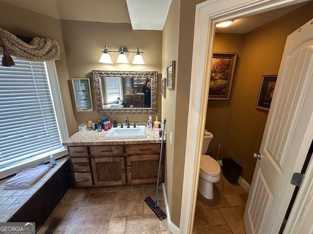 bathroom featuring baseboards, toilet, stone tile flooring, and vanity