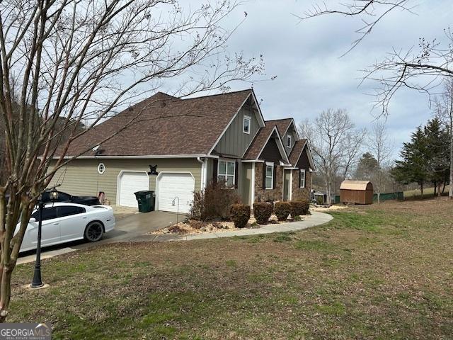 view of side of home featuring an attached garage, board and batten siding, a yard, stone siding, and driveway