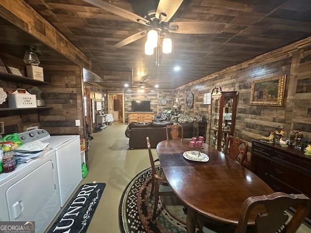 dining area with concrete flooring, wood walls, a ceiling fan, and washing machine and clothes dryer