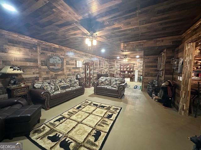 living area with wooden walls, wooden ceiling, concrete floors, and ceiling fan