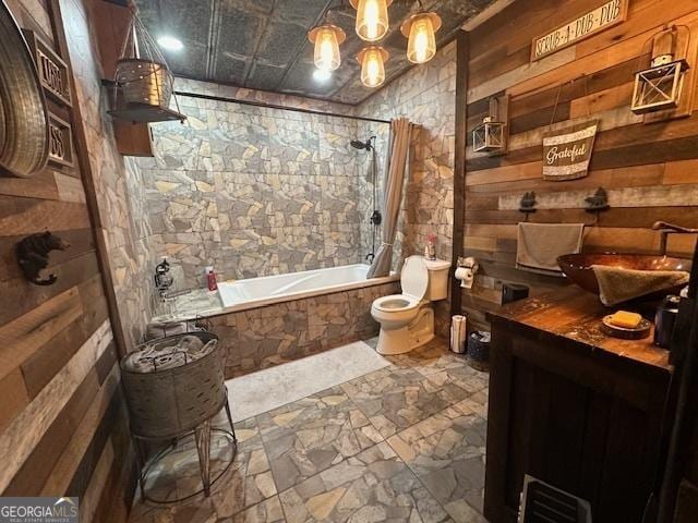 bathroom featuring wood walls, toilet, tiled shower / bath, and a sink