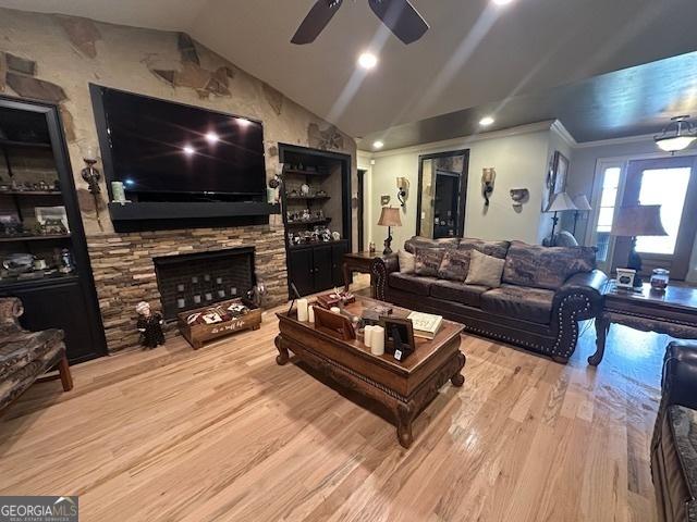 living room featuring ornamental molding, a ceiling fan, wood finished floors, a stone fireplace, and lofted ceiling