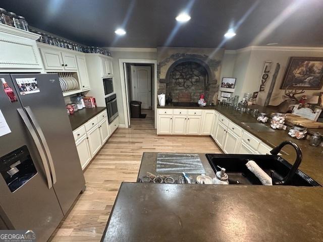 kitchen with light wood-type flooring, a sink, dark countertops, stainless steel fridge, and white cabinets