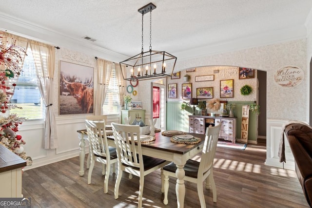 dining room featuring a textured ceiling, wood finished floors, wallpapered walls, wainscoting, and crown molding