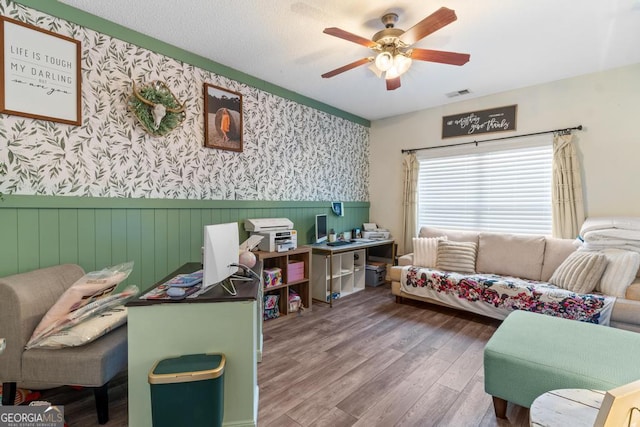 office space featuring visible vents, wallpapered walls, ceiling fan, a wainscoted wall, and wood finished floors