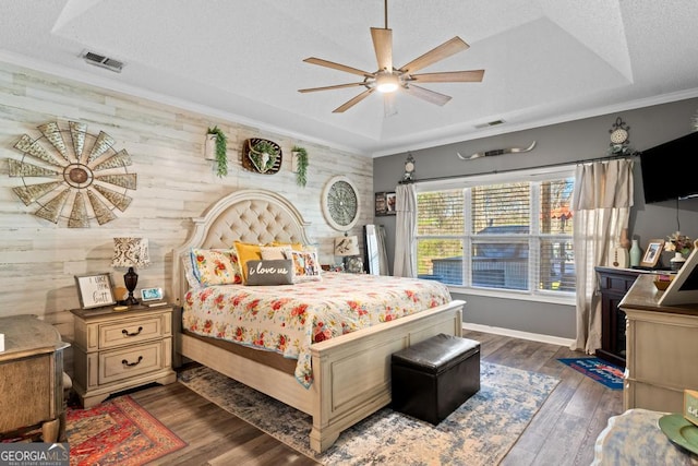 bedroom featuring visible vents, ornamental molding, a textured ceiling, a raised ceiling, and dark wood-style flooring