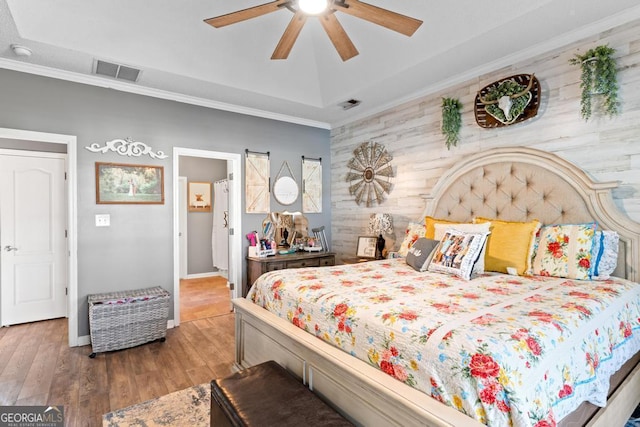 bedroom with visible vents, crown molding, an accent wall, wood finished floors, and a raised ceiling