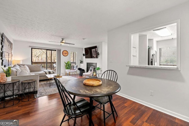 dining area with dark wood-type flooring, baseboards, a fireplace, a textured ceiling, and a ceiling fan