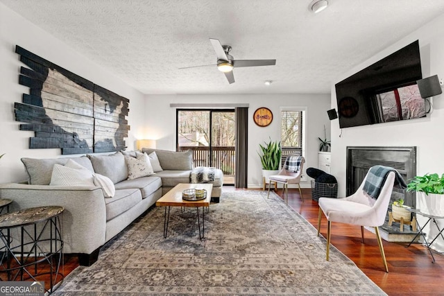 living area featuring wood finished floors, baseboards, a fireplace, ceiling fan, and a textured ceiling