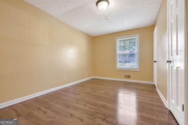 unfurnished bedroom featuring a textured ceiling, wood finished floors, visible vents, and baseboards