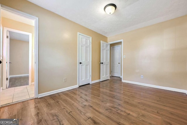 unfurnished bedroom with a textured ceiling, baseboards, and wood finished floors