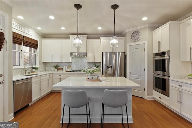 kitchen with a breakfast bar, a sink, under cabinet range hood, appliances with stainless steel finishes, and a center island