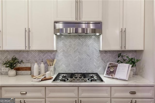 kitchen with decorative backsplash, stainless steel gas stovetop, wall chimney exhaust hood, and white cabinets