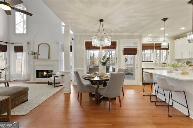 dining room with ornate columns, a fireplace with flush hearth, light wood finished floors, and ornamental molding