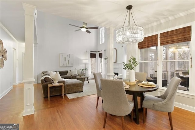 dining space featuring ceiling fan with notable chandelier, decorative columns, wood finished floors, and baseboards